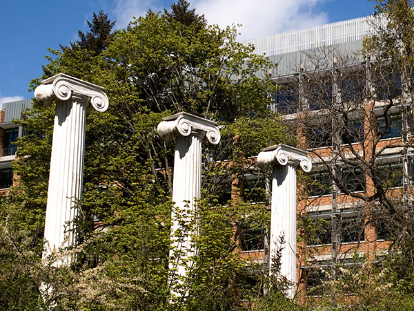 Sylvan Grove columns surrounded by tree foliage with Allen Center, a six-story building of orange brick with windows shaded by metal ledges, in the background