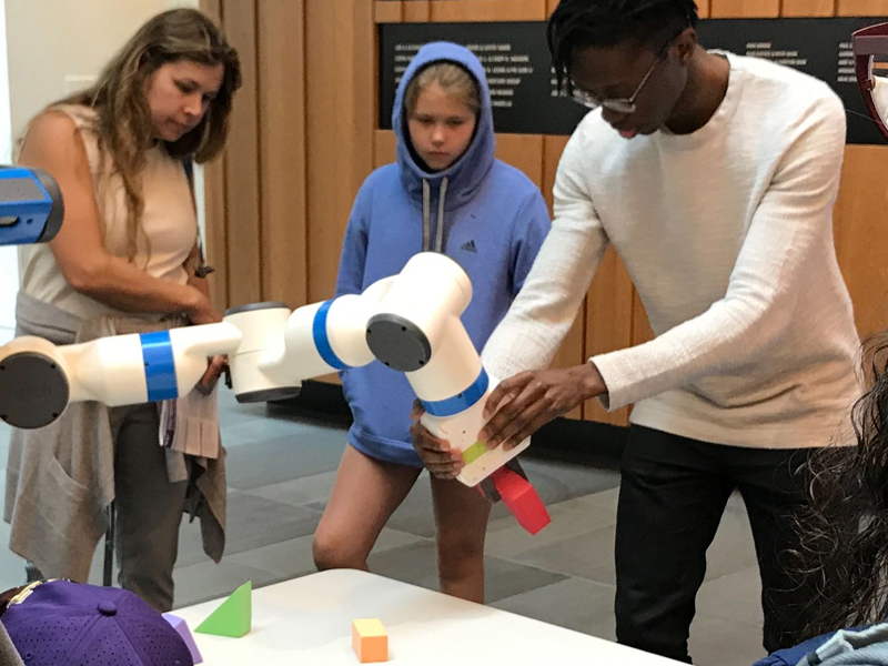 Young man adjusting the position of robotic arm while students watch.