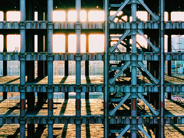 Metal scaffolding of a skyscraper under construction with sunlight peeking through on the horizon