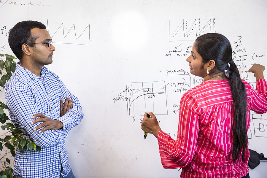 Allen School graduate student Rajalakshmi Nandakumar discusses her research on sonar technology for collecting sleep data while pointing to information written on a whiteboard.