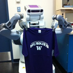 A robot holding up a purple UW Huskies t-shirt