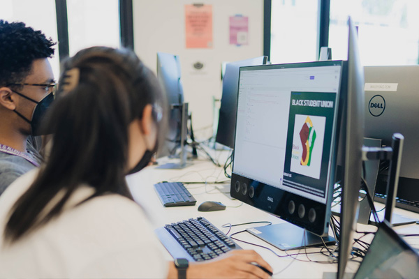 Student Engagement & Access photo featuring students sitting at a desk with compute screens