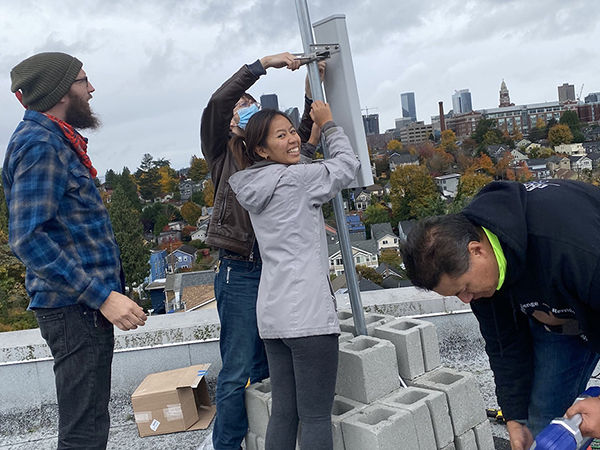 A group of four students erect community broadband networking apparatus on a rooftop