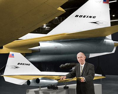 Maynard Pennell posing with model Boeing aircraft in front of full sized version inside a brightly lit hangar