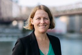 Portrait of Nicola Dell standing outside with a bridge and water in the background