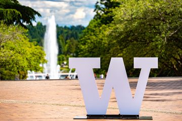 The University of Washington "W" sits at the foreground with the Drumheller Fountain spouting in the background