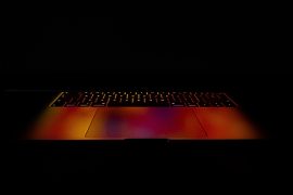 Dark and ominous image of partially open laptop with a faint reddish-orange glow