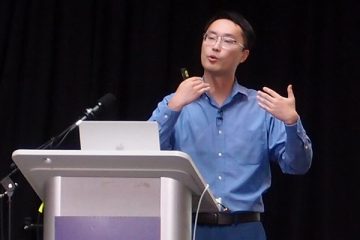 Sheng Wang speaking at a podium