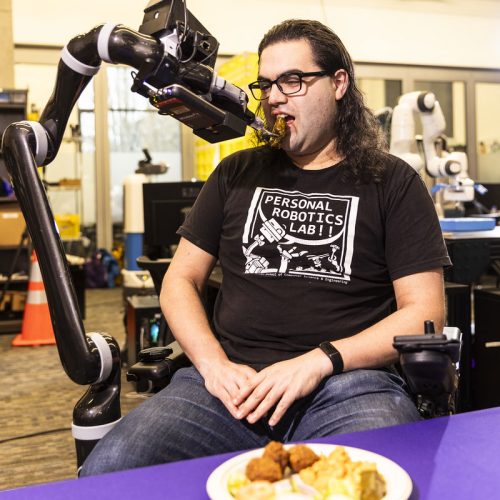 Image of a robot feeding arm assisting a person in a wheel chair